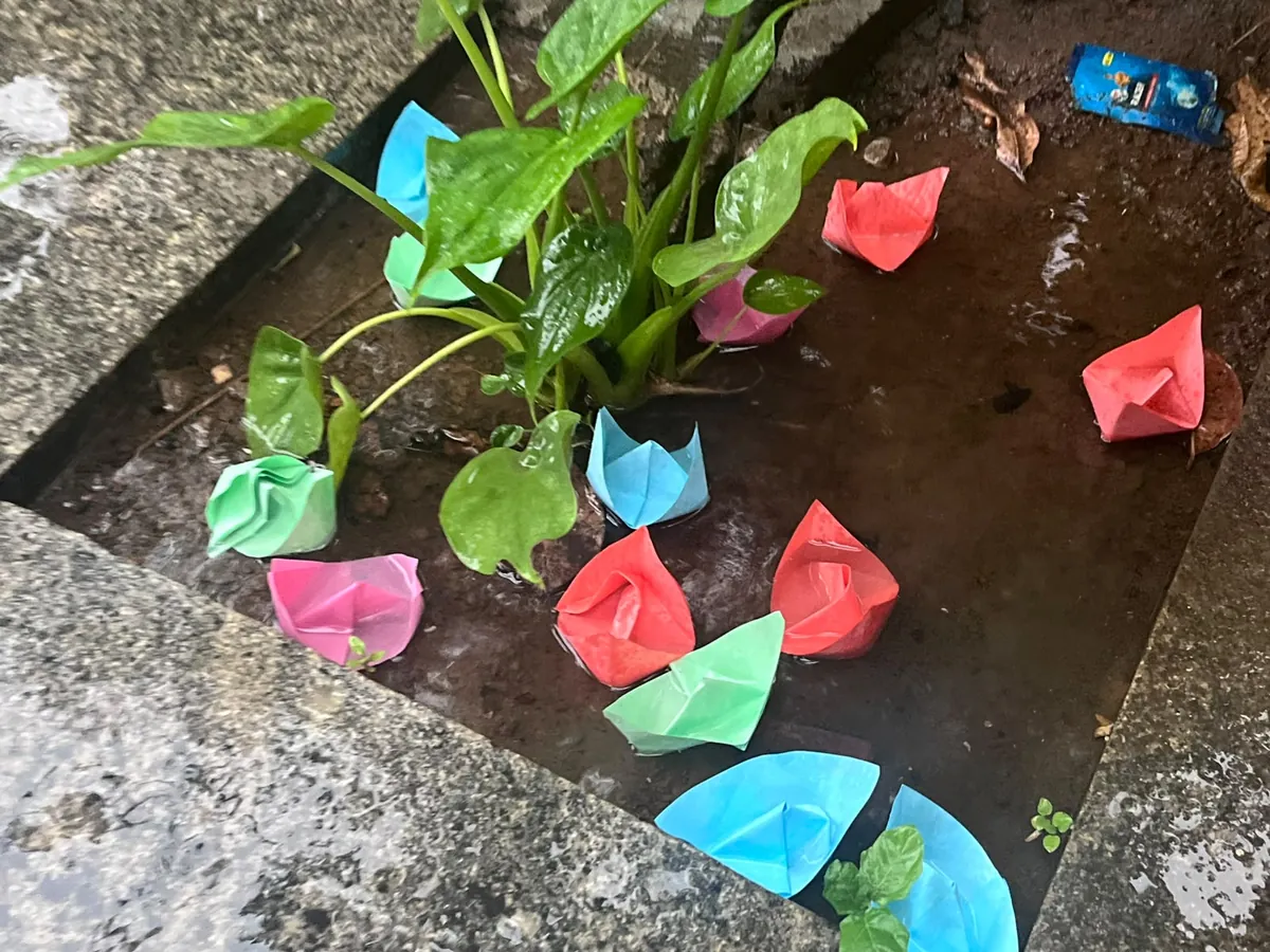 Paper boats folded by children floating in a puddle during a hands-on science challenge